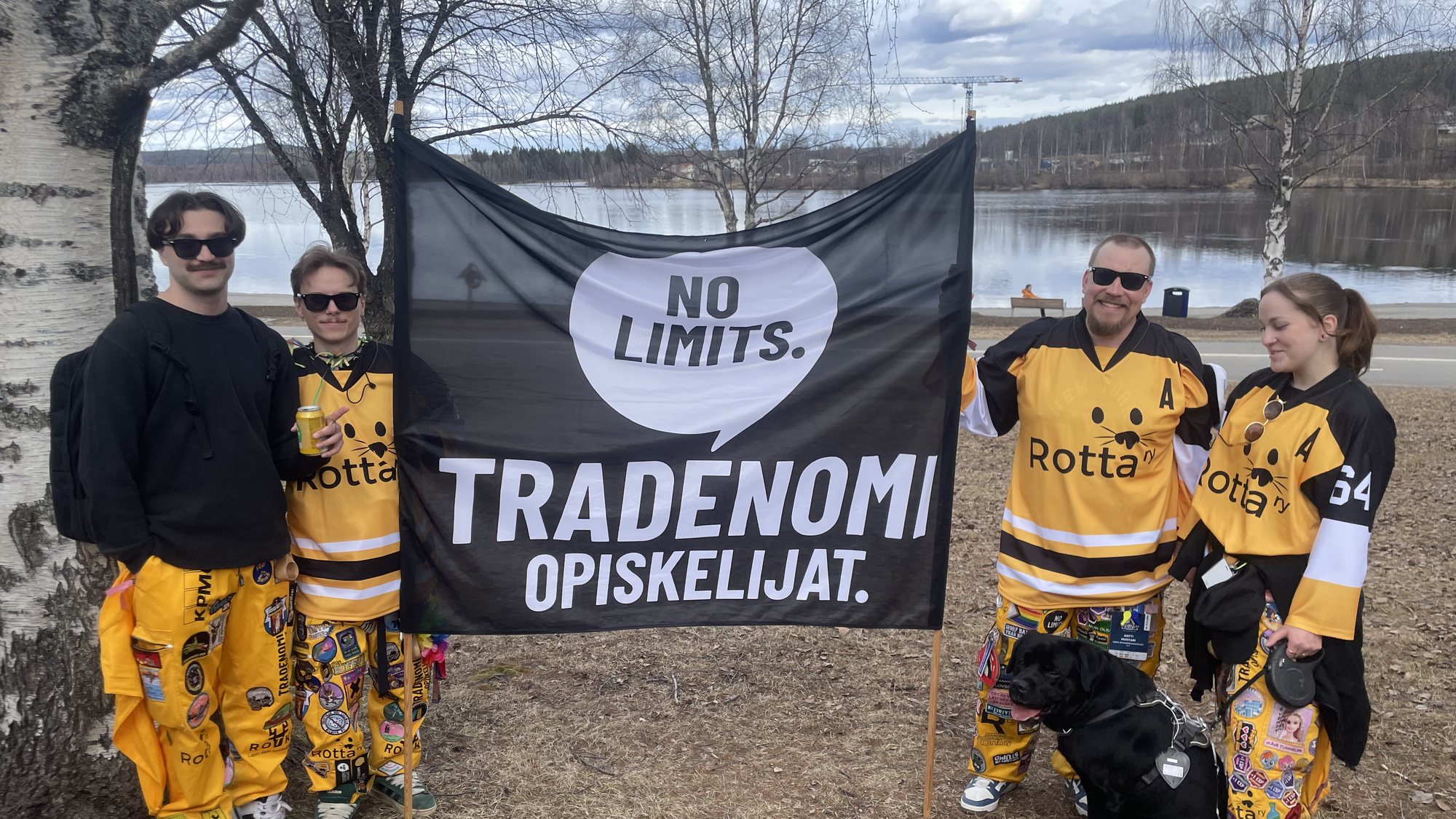 ROTTA ry:n jäseniä keltaisissa pelipaidoissa ja haalareissa Tradenomiopiskelijoiden lipun ääressä joen rannalla.