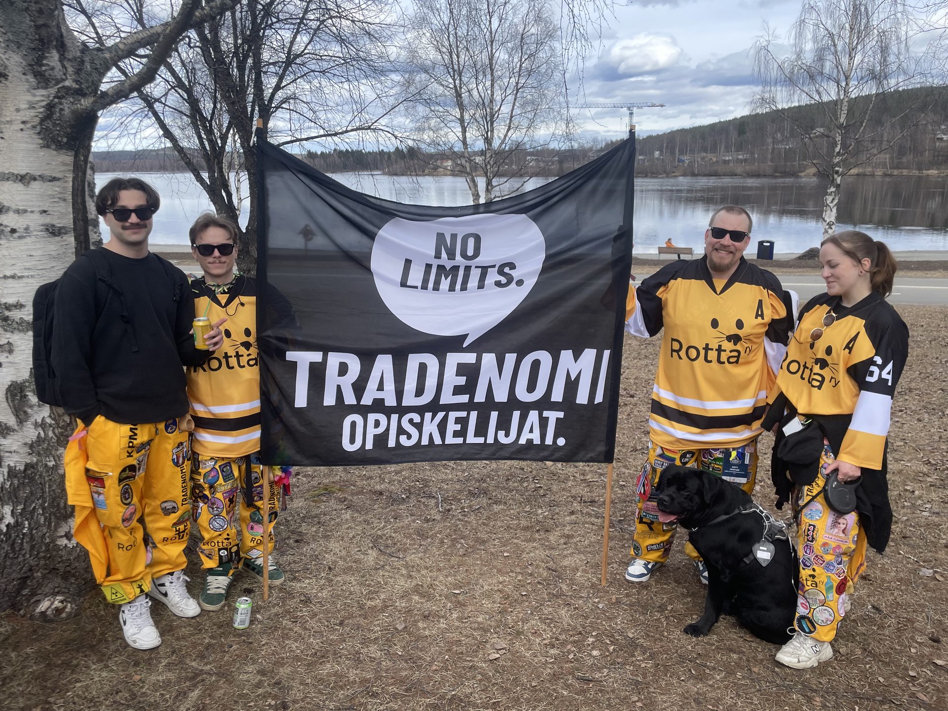 Neljä ROTTA ry:n jäsentä keltaisissa pelipaidoissa ja merkkien peittämissä haalareissa Tradenomiopiskelijoiden lipun ääressä.