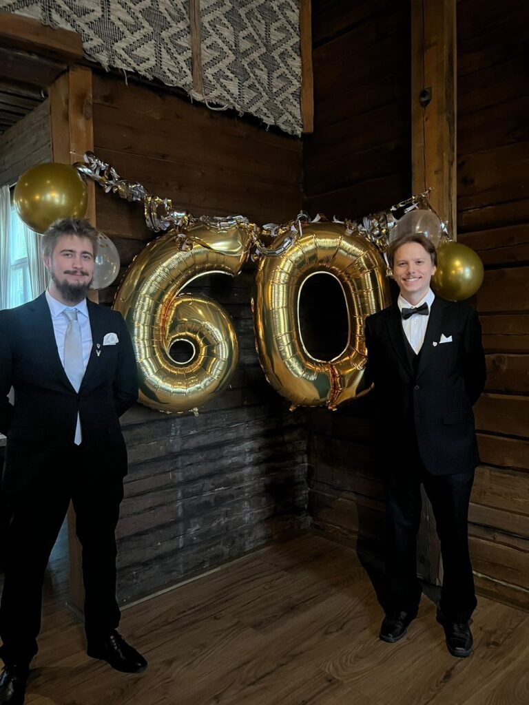 Jere ja Tommi juhlapuvuissa Rovaniemen Metsäpoikien 60-vuotisjuhlilla, taustalla kultaiset 60-ilmapallot.